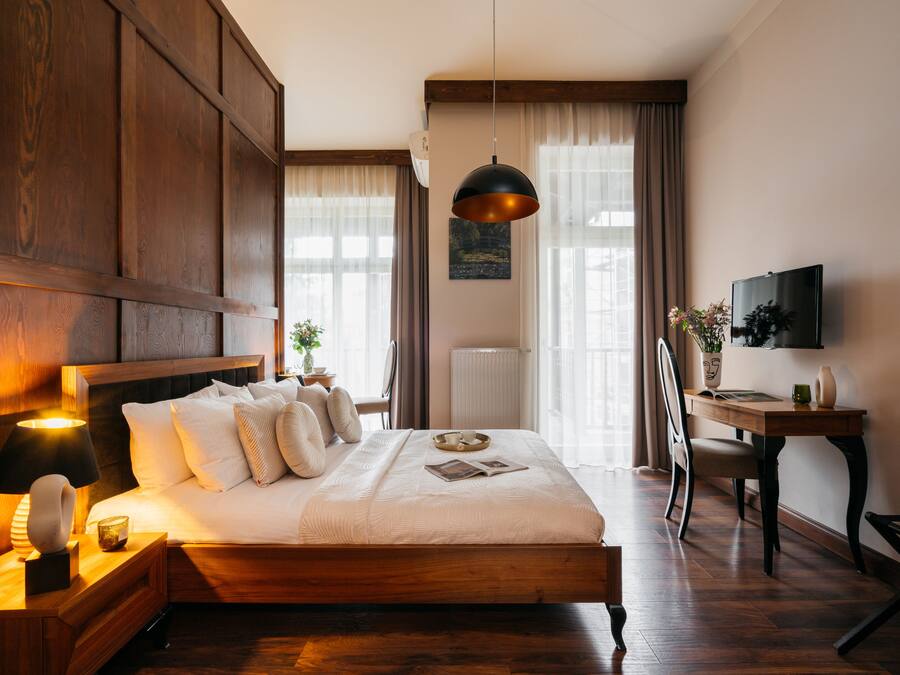 A well-lit bedroom with a wooden bed, bedside table, and a desk with a chair.