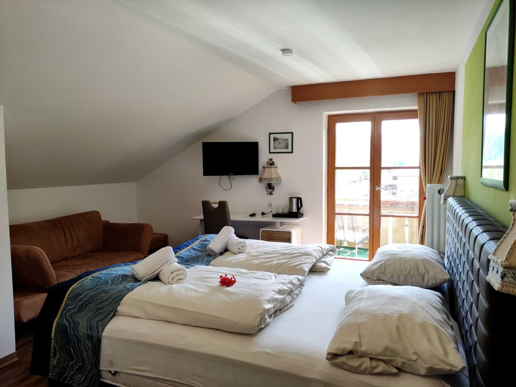A hotel room with two beds, a sofa, a desk with a TV, and a window with curtains.