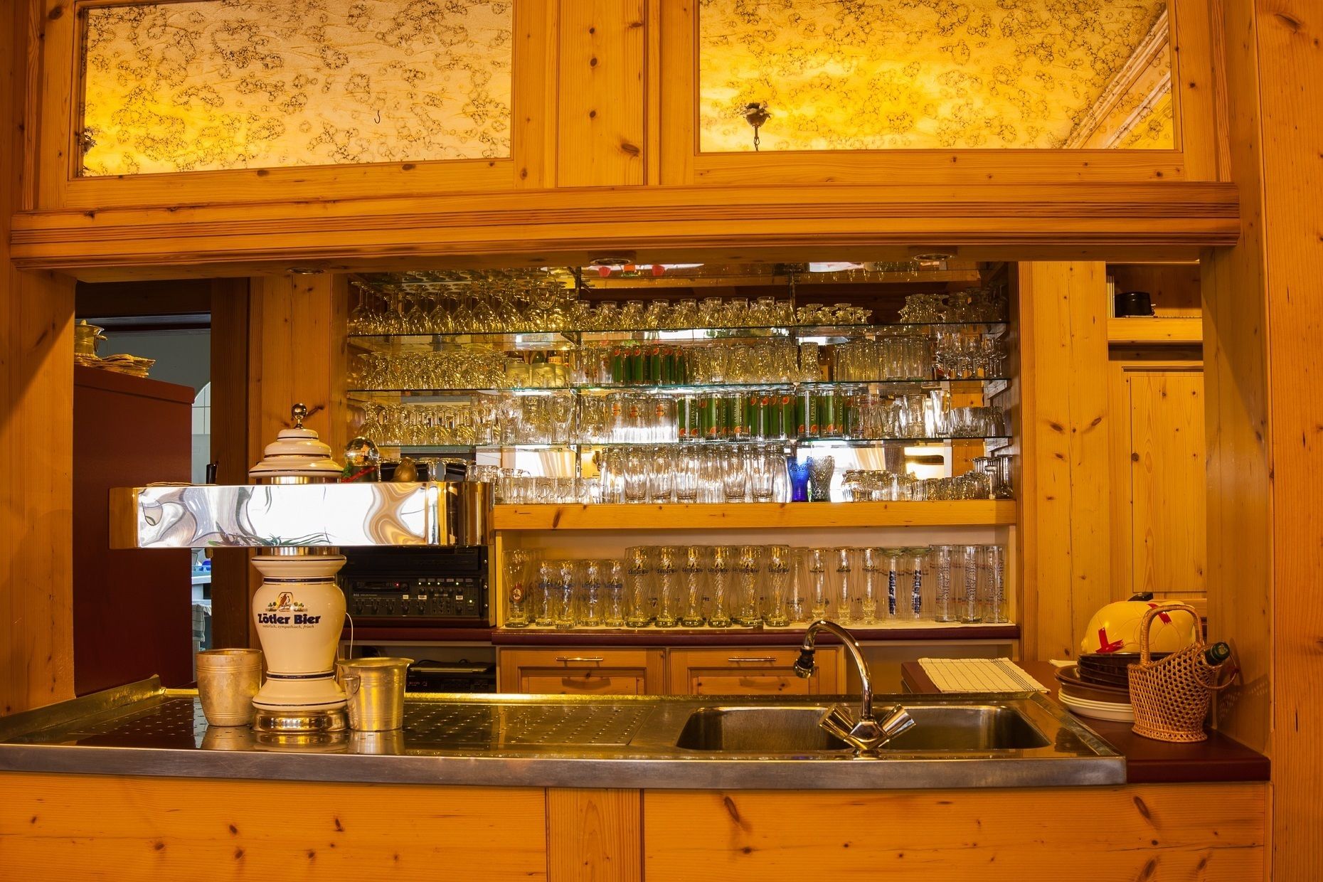 A bar area with wooden paneling, a sink, and shelves stocked with glassware.