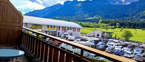 A mountain view from a balcony with a parking area and a building with a yellow facade.