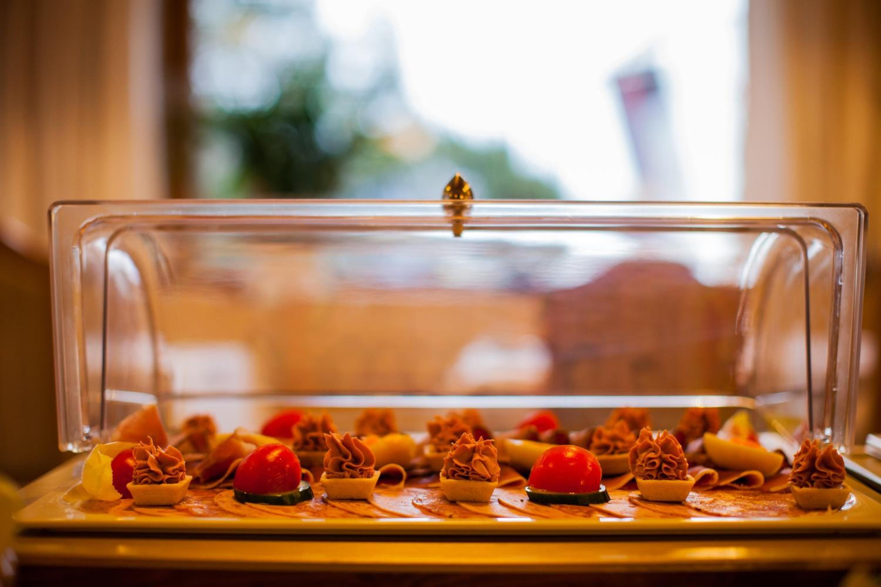 Un buffet proposant une variété de plats, notamment de petites pâtisseries, le tout présenté sous une cloche en verre transparente.