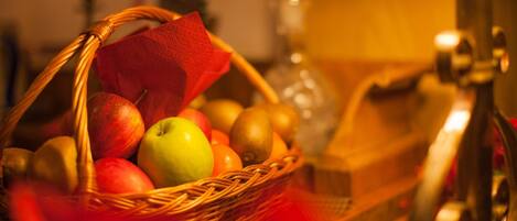 A wicker basket filled with various fruits, including apples and oranges, placed on a surface with a red cloth.
