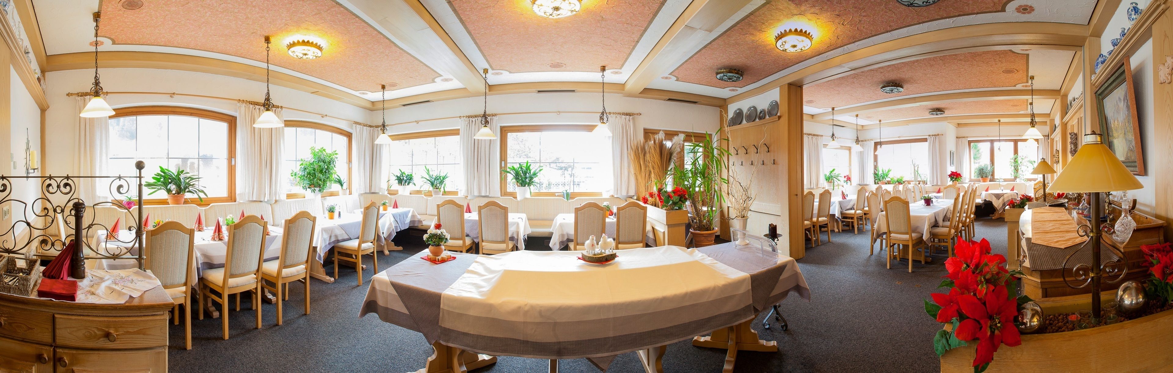 Een ruime eetruimte met ronde tafels en stoelen, grote ramen en plafondlampen.