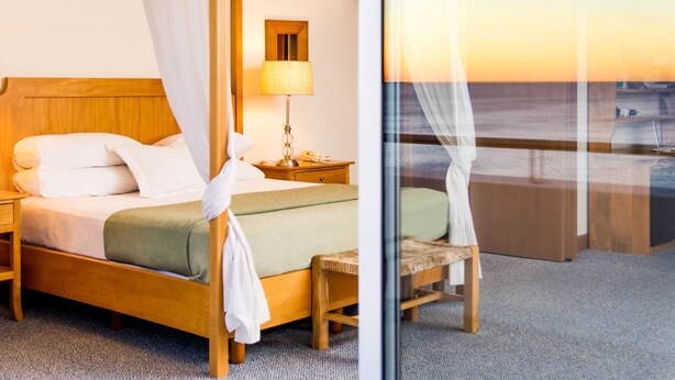 Habitación de hotel con cama, mesita de noche, lámpara, silla y vista a la playa a través de una puerta de cristal.