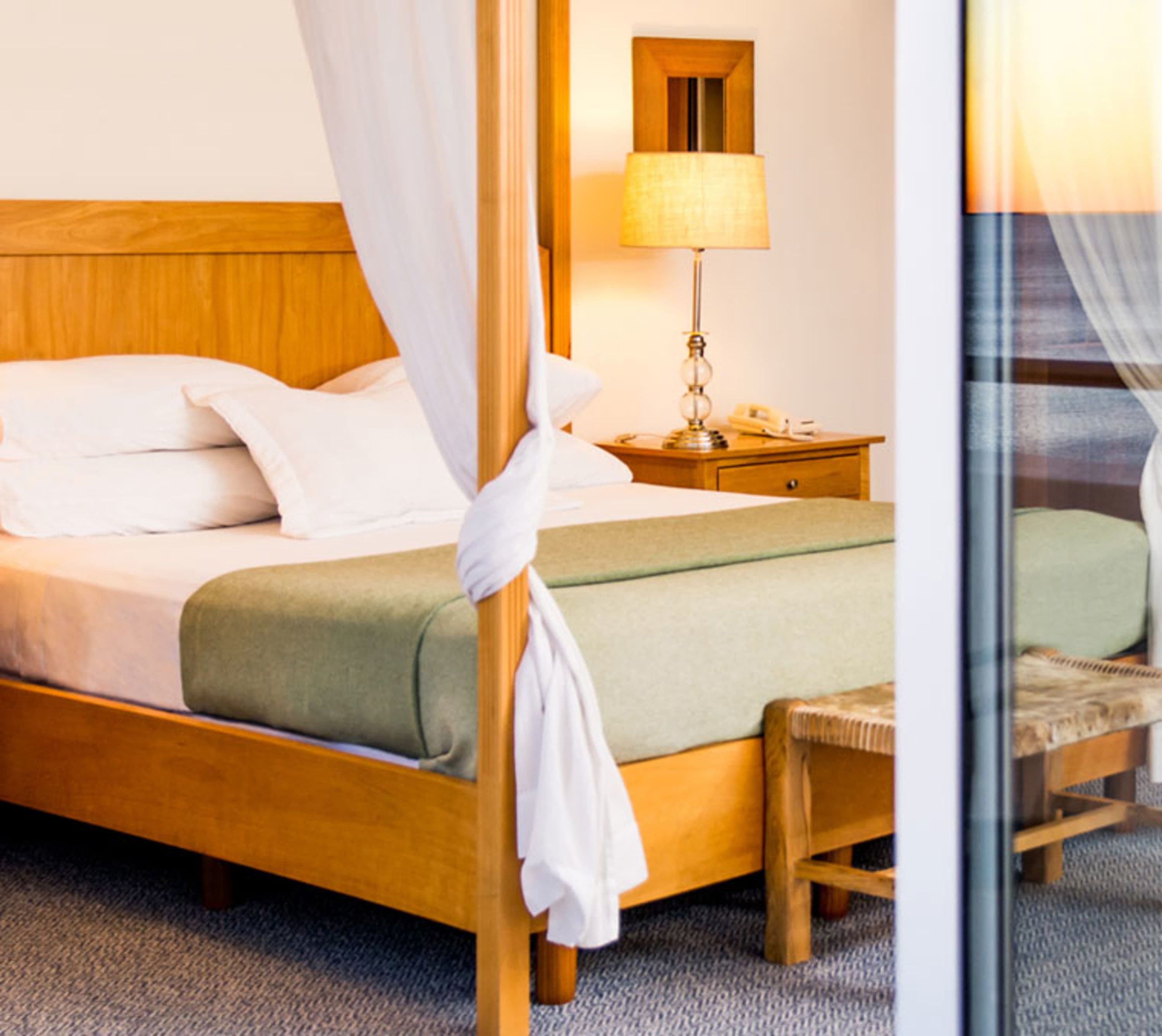 A four-poster bed with a canopy, a bedside table with a lamp, and a chair.