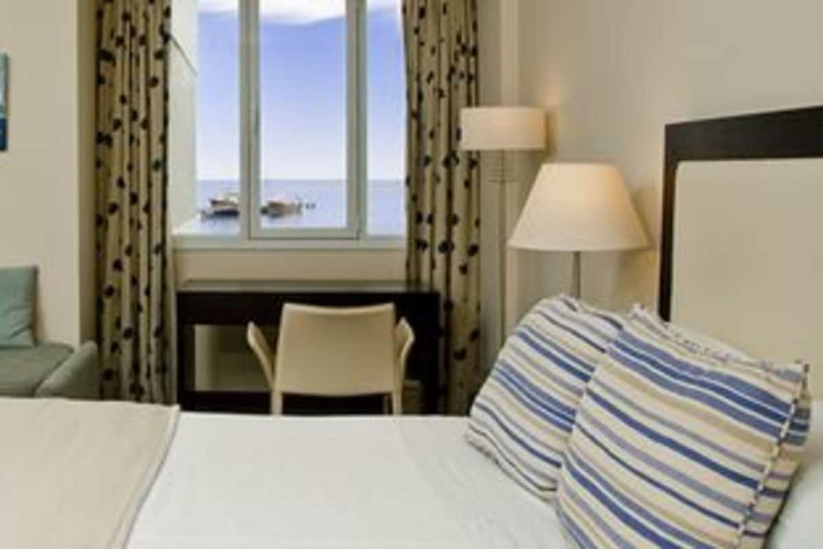 A hotel room with a bed, a sofa, a desk, and a view of the sea.