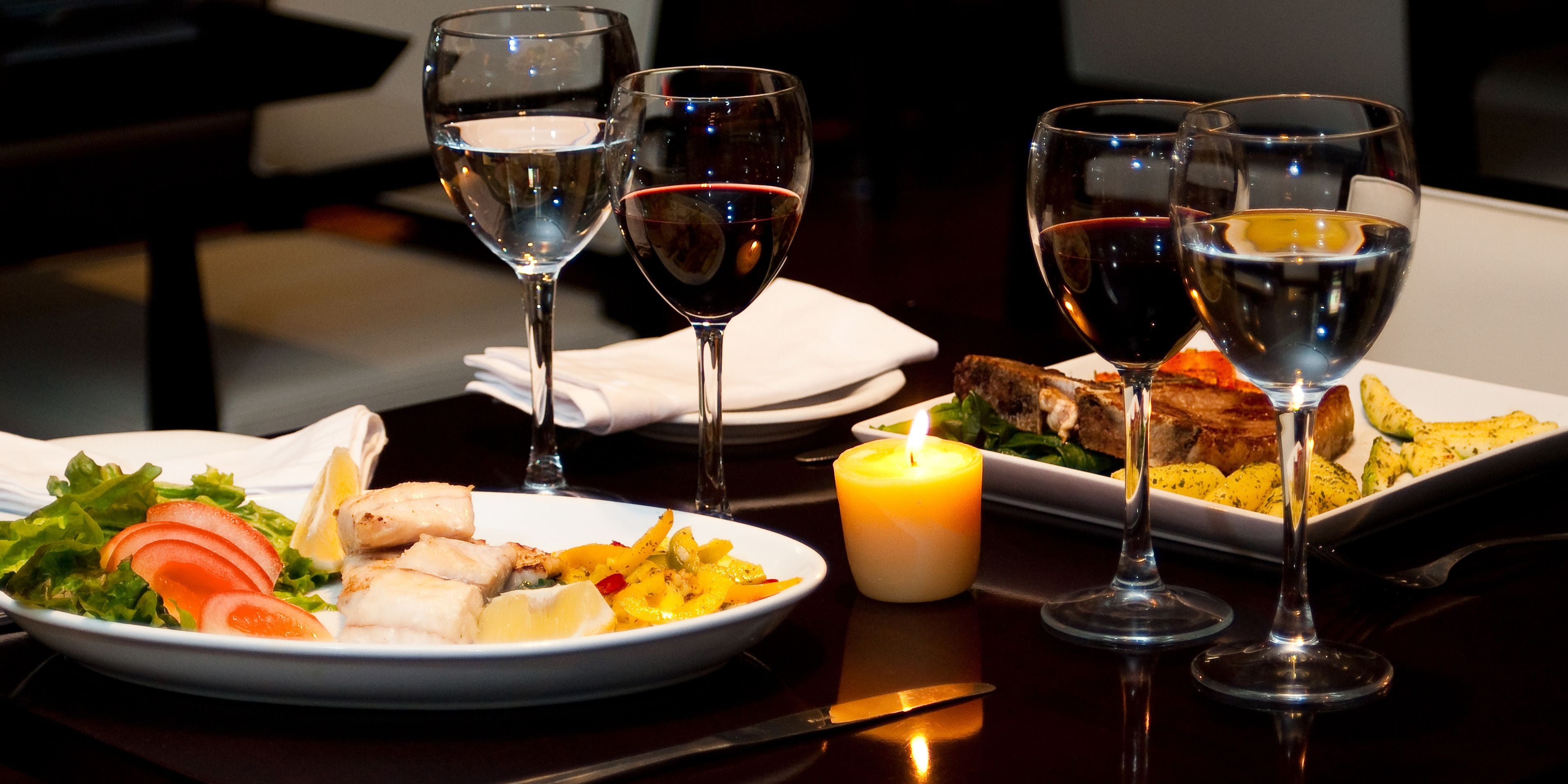 A dining table with plates of food, wine glasses, and a lit candle.
