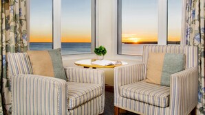 Una habitación con dos sillones a rayas, una mesita con un libro y una planta, y vistas al atardecer sobre el océano.