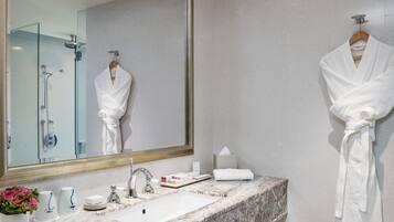 A modern bathroom with a marble sink, a large mirror, a robe hanging on the wall, and a glass shower enclosure.