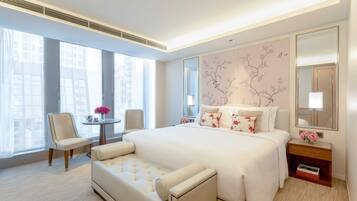 A modern hotel room with a large bed, a sofa, a small table with flowers, and a large mirror.