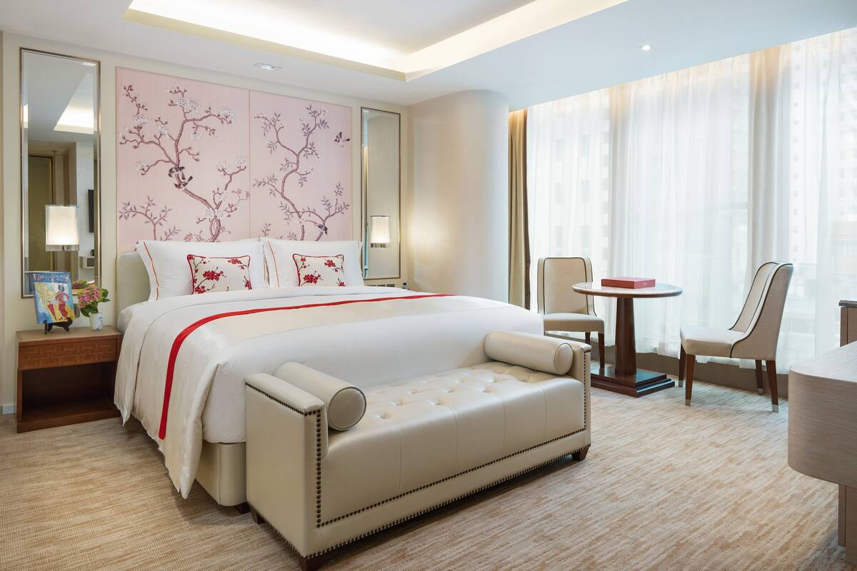 A hotel room with a large bed, a sitting area with a chair and table, a mirror, and a decorative wall.