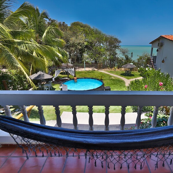 A pool area with a view of the ocean, surrounded by lush greenery and a white building. - Pousada Enseada dos Golfinhos (Tibau do Sul)