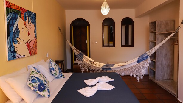 Un dormitorio con cama, una hamaca, un candelabro y un cuadro en la pared.