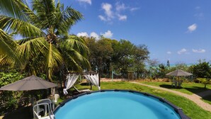 An outdoor swimming pool surrounded by palm trees and greenery, with lounge chairs and umbrellas. - Pousada Enseada dos Golfinhos (Tibau do Sul)