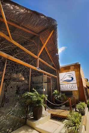 A building with a thatched roof, a sign reading "Pousada Enseada dos Golfinhos", and a rope barrier with potted plants. - Pousada Enseada dos Golfinhos (Tibau do Sul)
