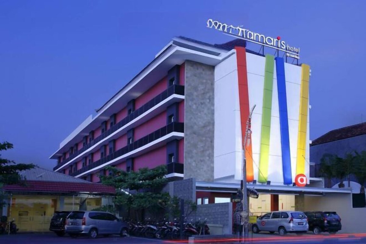 A multi-story hotel with a prominent vertical sign featuring a rainbow pattern and the name 'Tamaris Hotel'.