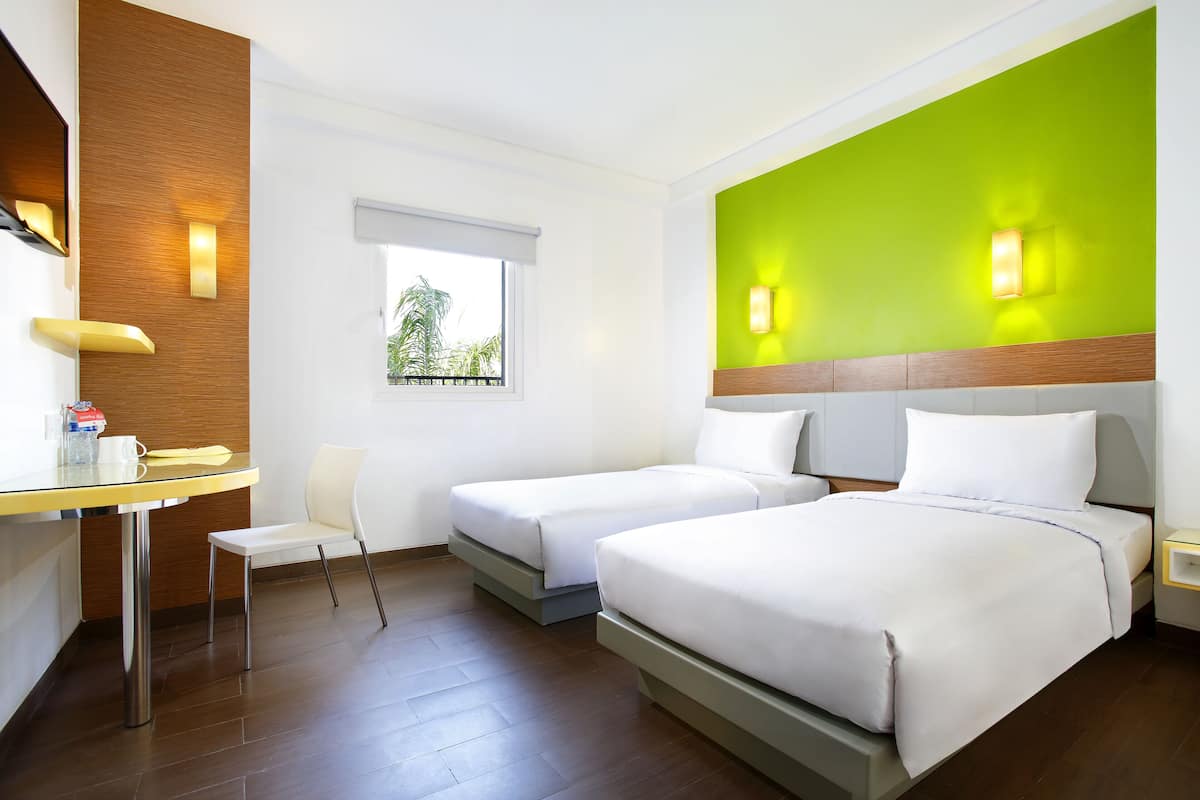 Habitación de hotel con dos camas, un escritorio, una silla y un ventanal con vistas a zonas verdes.