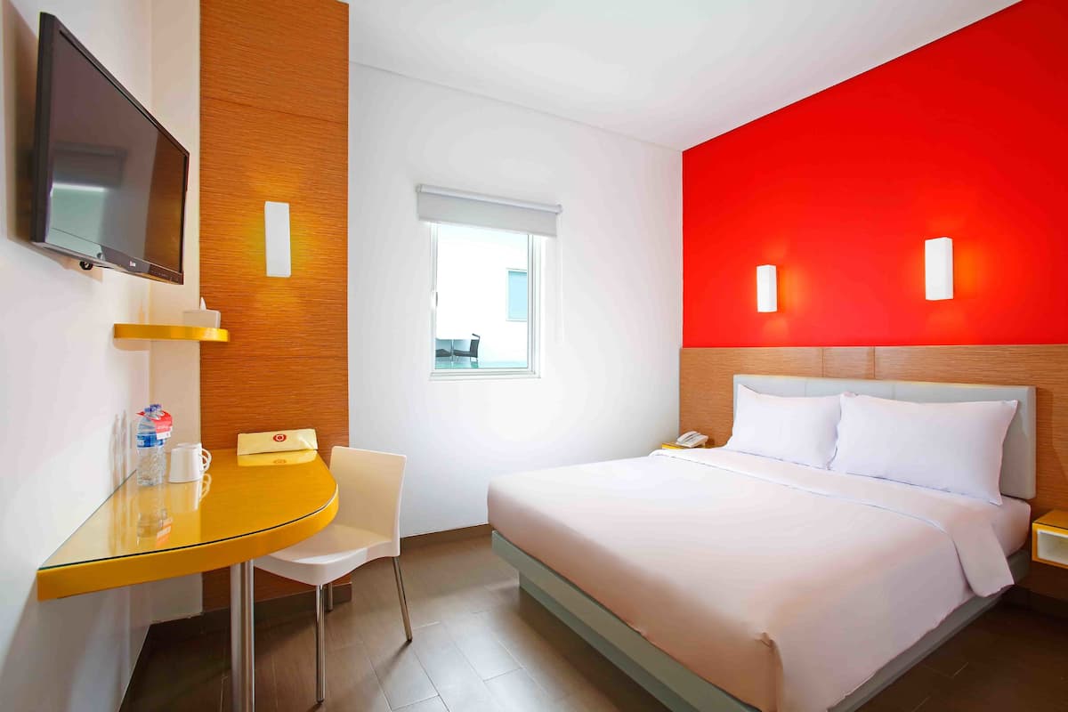 Habitación de hotel con cama, escritorio, silla, televisor y ventana.