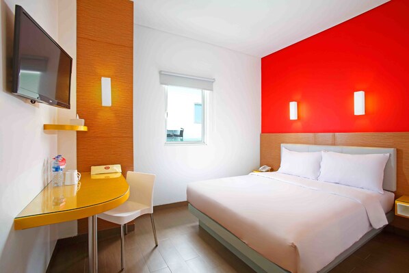 A hotel room with a bed, a desk, a chair, a TV, and a window.