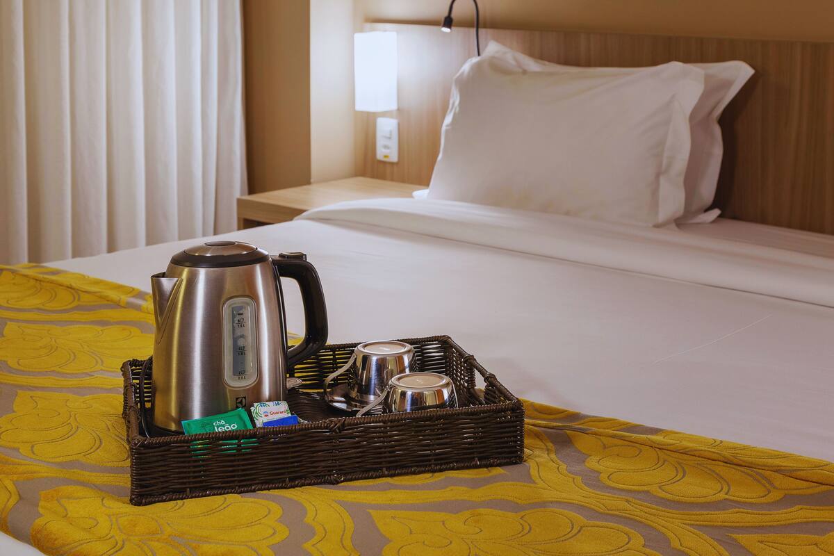 Ein Hotelzimmer mit einem Bett, einem Nachttisch, einer Lampe, einem Wasserkocher und einem Tablett mit Tassen und einem Teebeutel.