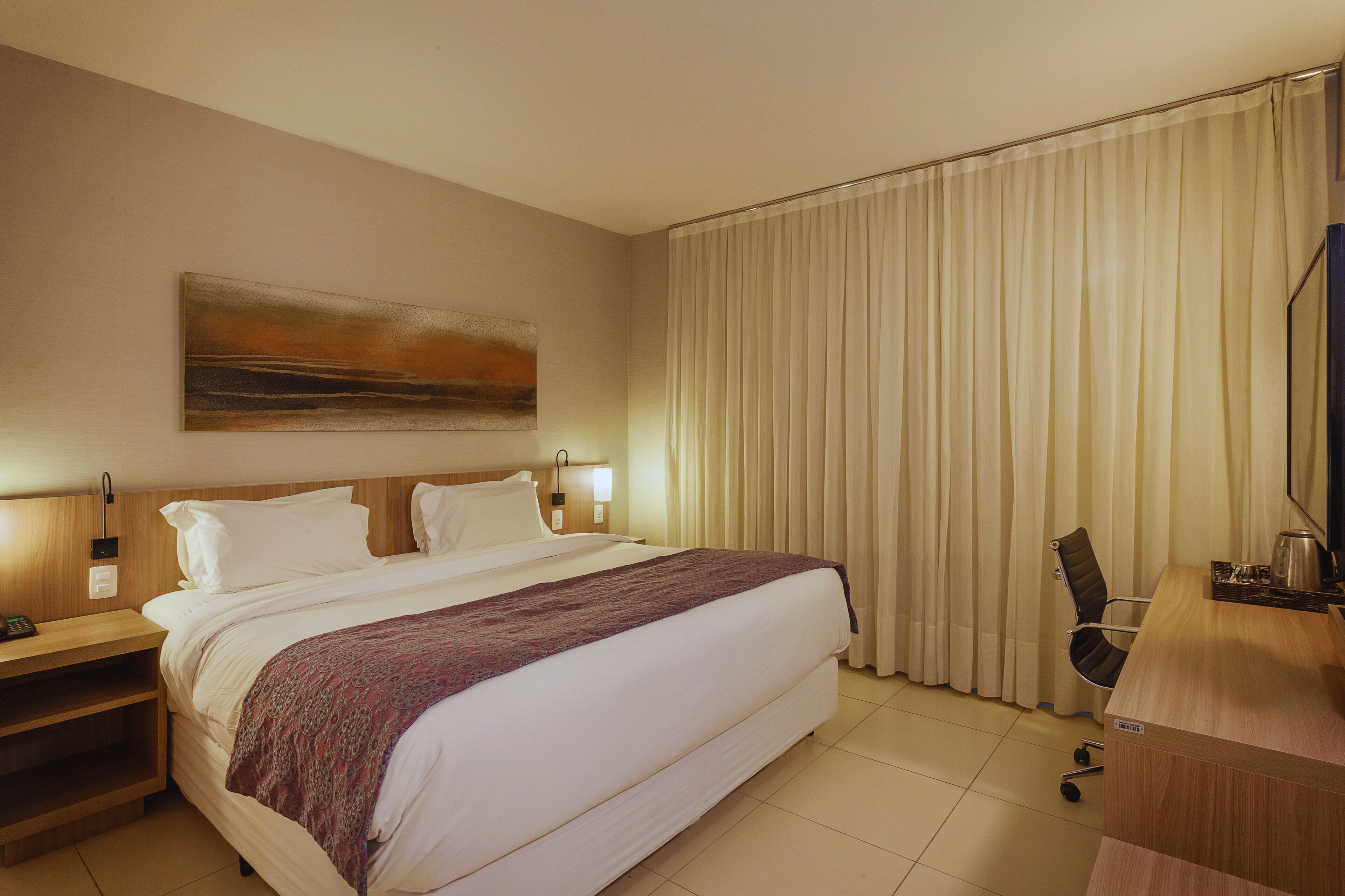 A hotel room with a large bed, a desk, a chair, and a television.