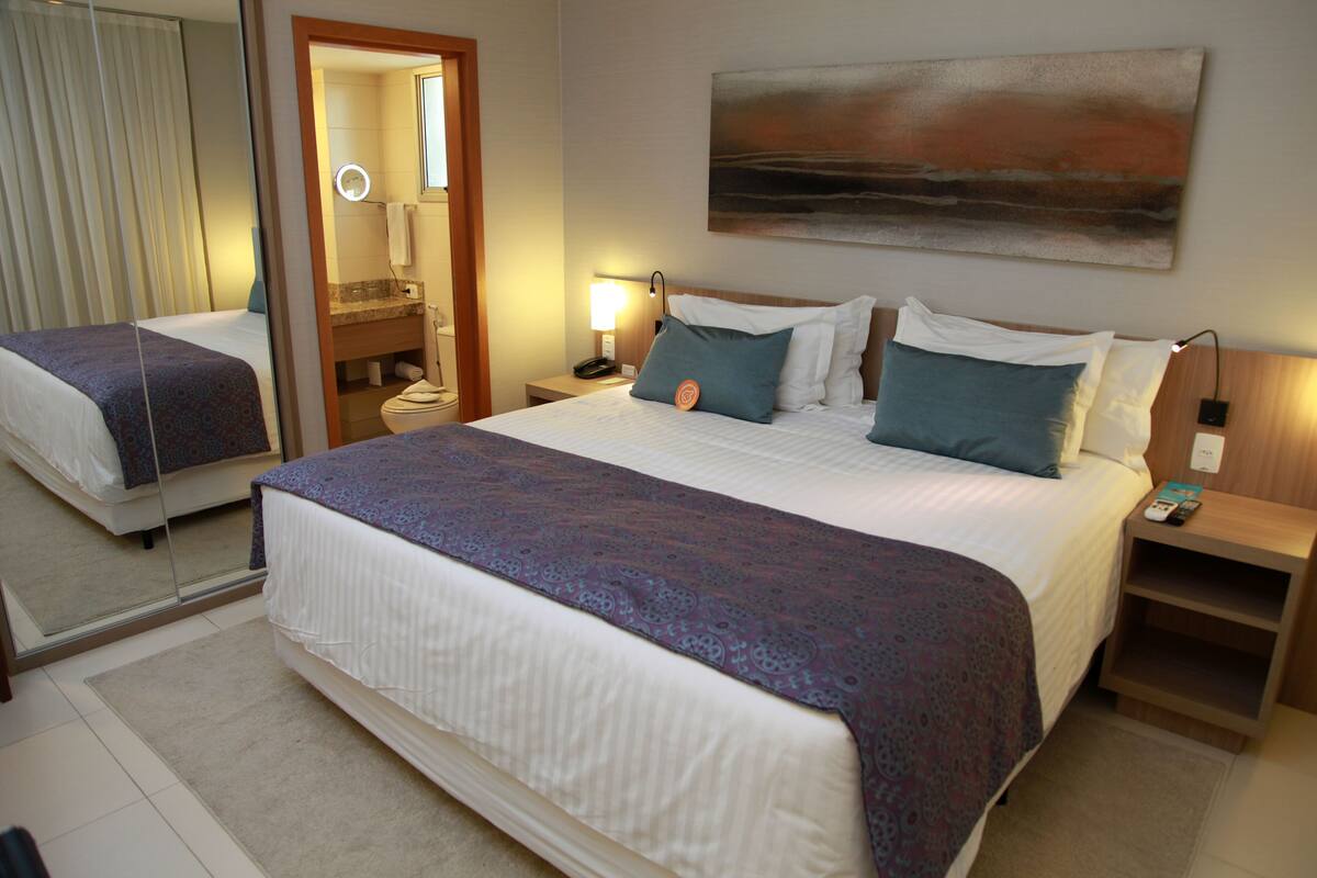Une chambre d’hôtel avec un grand lit, une table de chevet avec une lampe, un miroir et un tableau au mur.