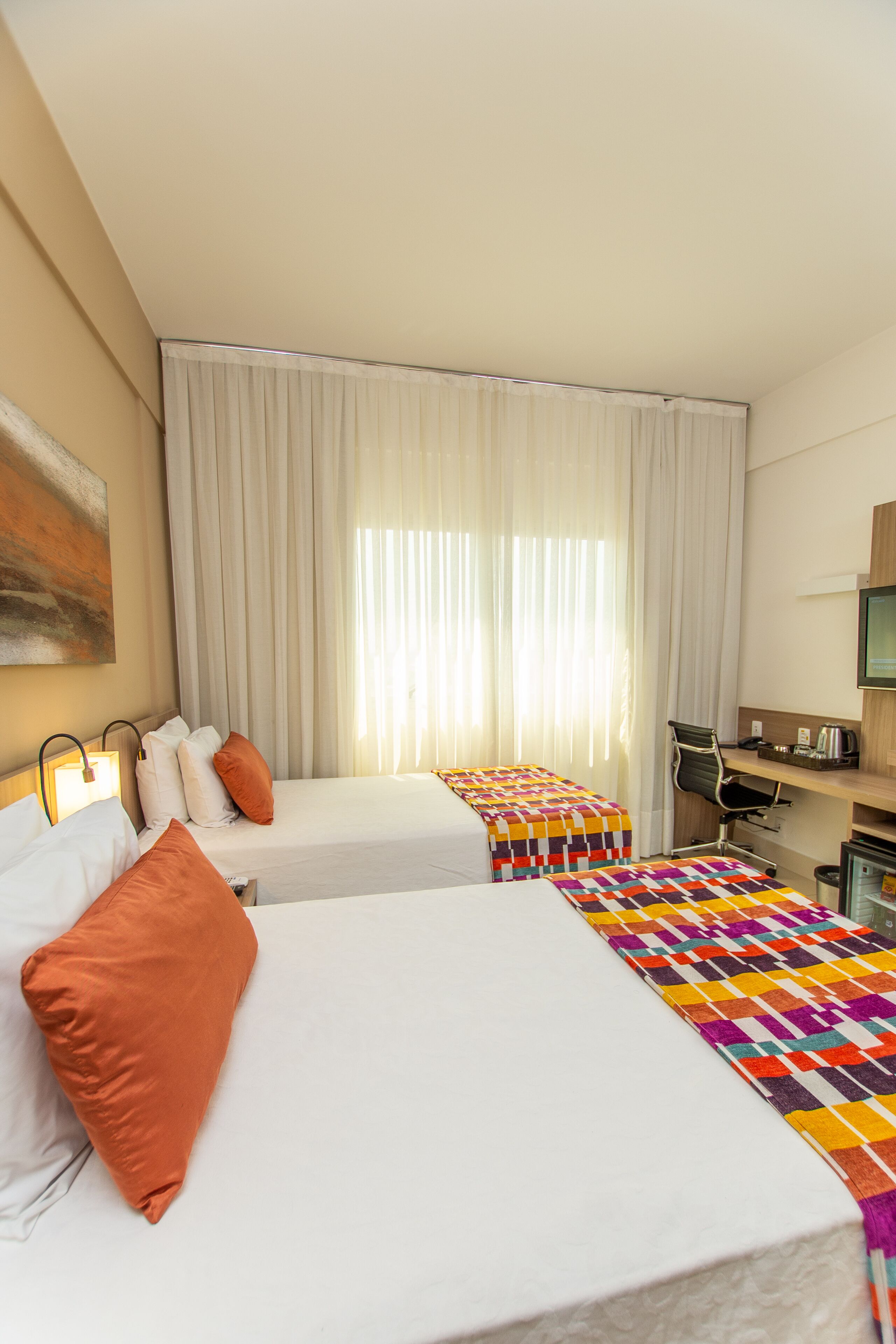 A hotel room with two beds, a desk, a chair, and a television.