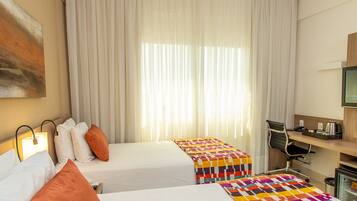 A hotel room with two beds, a desk, a chair, and a television.