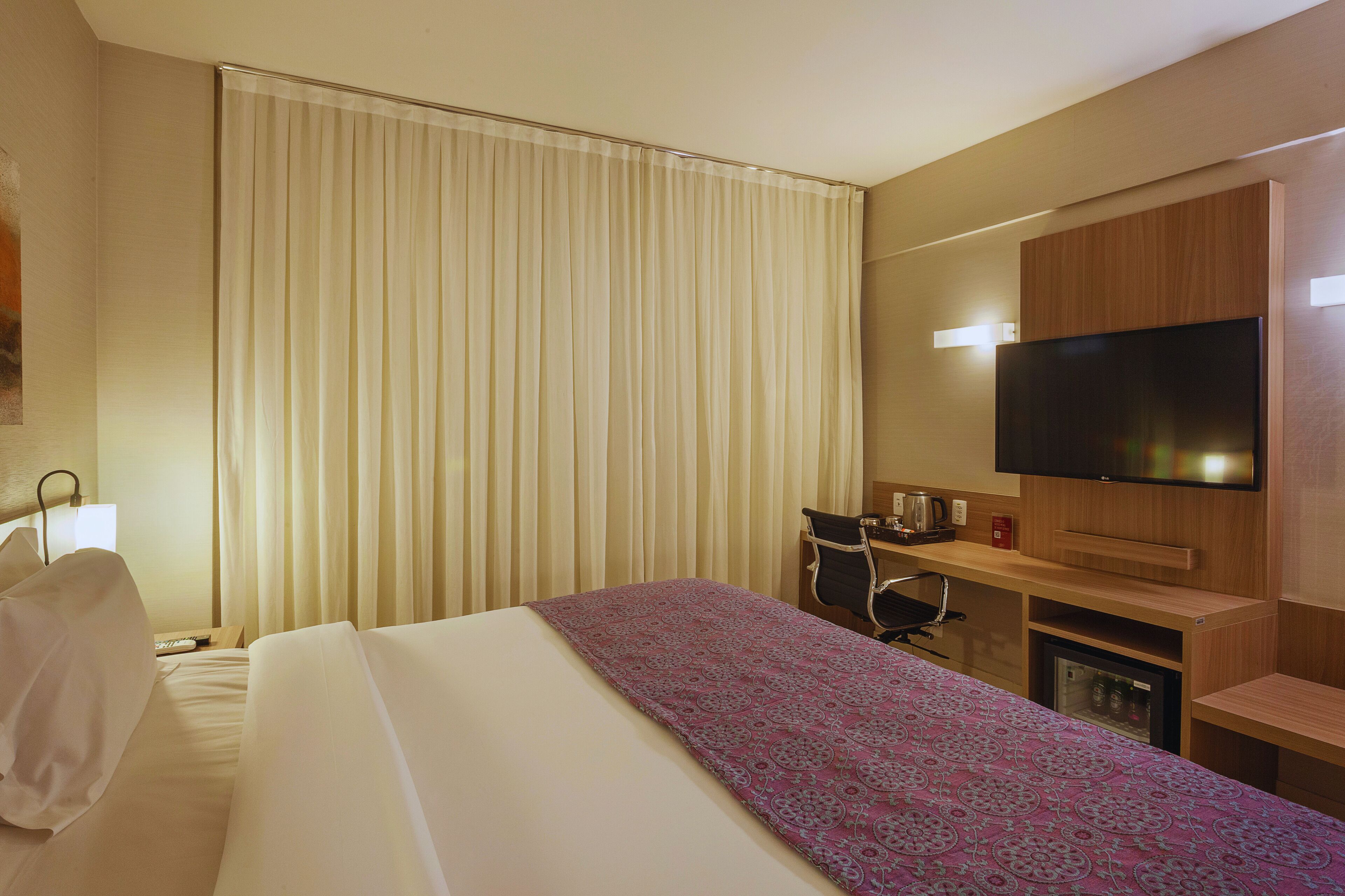 A hotel room with a bed, a desk, a television, and a minibar.