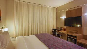 A hotel room with a bed, a desk, a television, and a minibar.