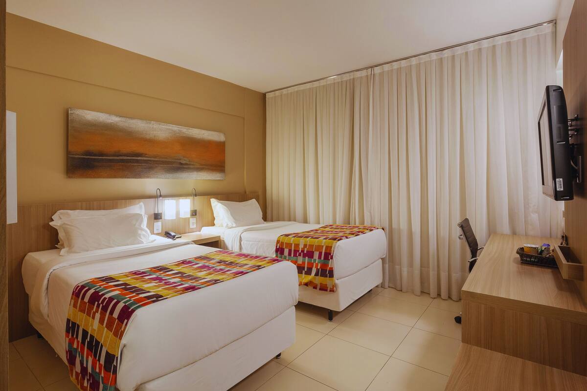 Ein Hotelzimmer mit zwei Betten, einem Schreibtisch, einem Fernseher und einem Bild an der Wand.