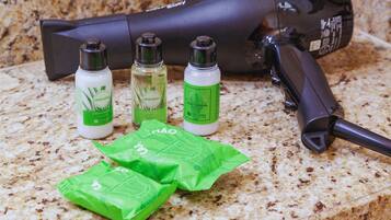 A hairdryer, three bottles of hair care products, and two green packets on a granite countertop.