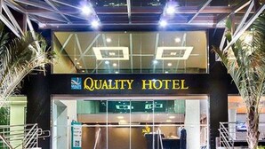 Das Außereinsehen eines Hotels namens "Quality Hotel" mit modernem Design, das einen markanten Eingang mit Glastüren, eine zur Eingangstür führende Treppe und Palmen an beiden Seiten des Eingangs zeigt.