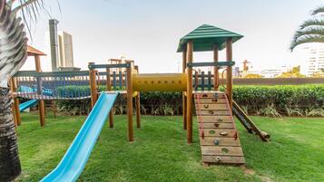 Un parque infantil con un tobogán azul, una red de escalada y estructuras de madera para trepar.
