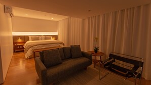 Ein Hotelzimmer mit einem Bett, einem Sofa, einem kleinen Tisch mit Pflanze, einer Bank und einer Wandklimaanlage.