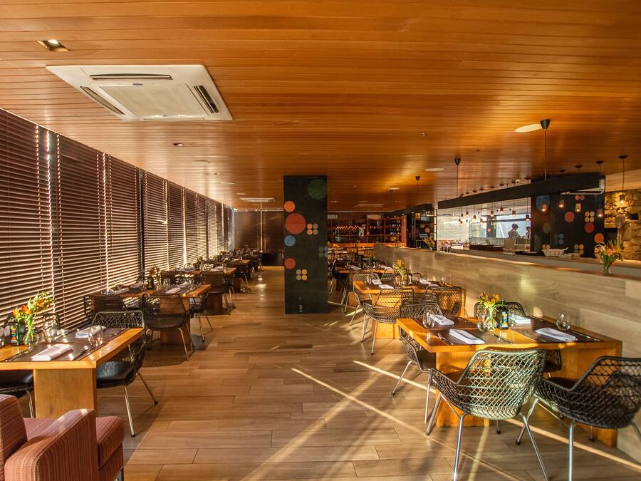 A spacious restaurant with wooden floors and a long counter. Tables are arranged for dining, and there are chairs with metal frames.