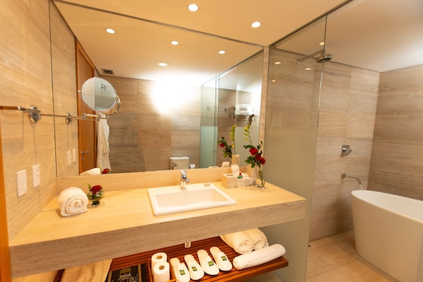 Un baño moderno con un lavamanos grande, espejo y bañera. Hay toallas y artículos de aseo en la encimera.