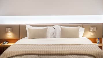 A neatly made bed with a beige comforter and pillows, a bedside table with a lamp, and a wall-mounted phone.