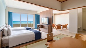 Ein Hotelzimmer mit zwei Betten, einem Fernseher, einem Esstisch und Blick aufs Meer.