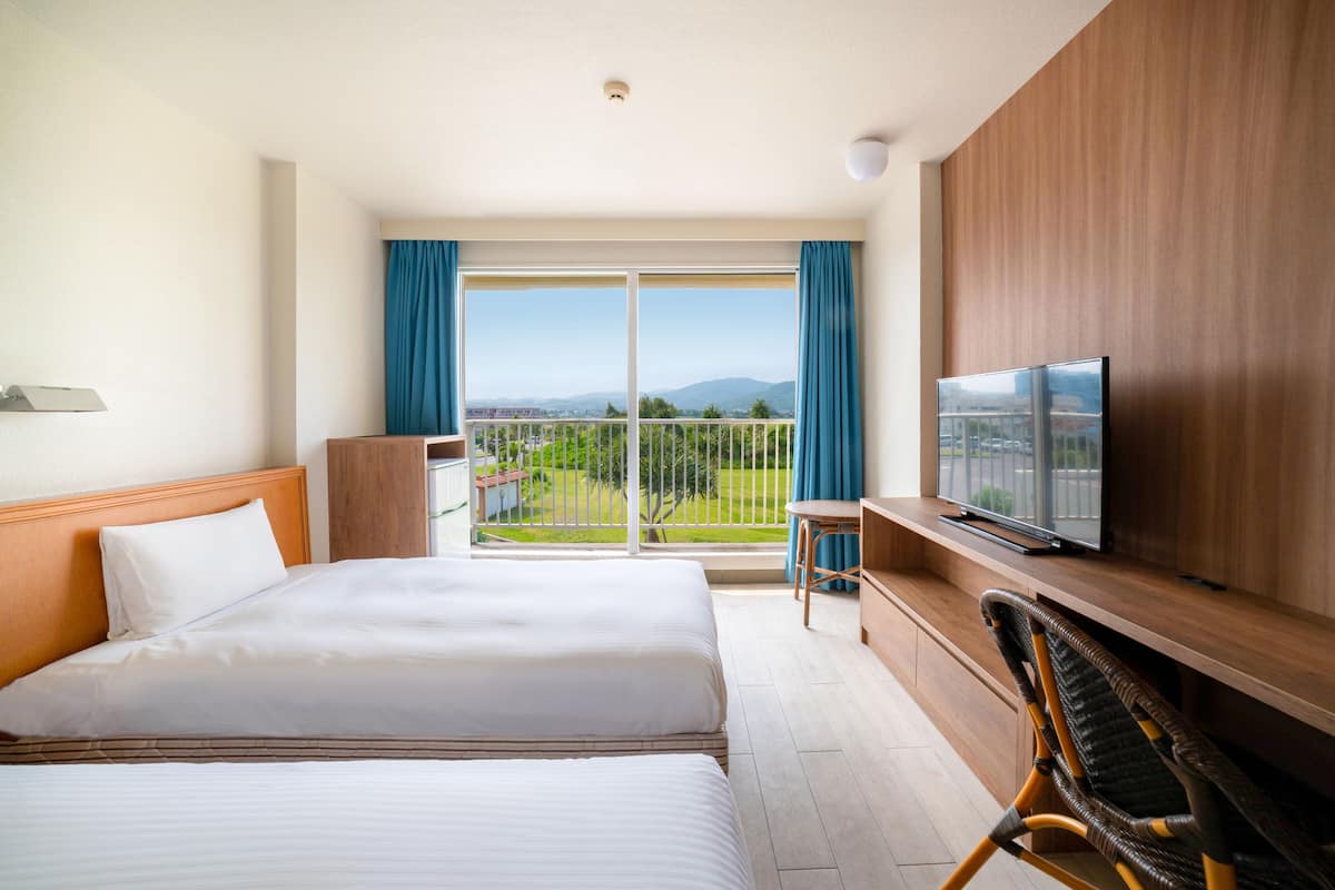 Habitación de hotel con una cama grande, televisor, balcón con vistas a la ciudad y un escritorio de madera.