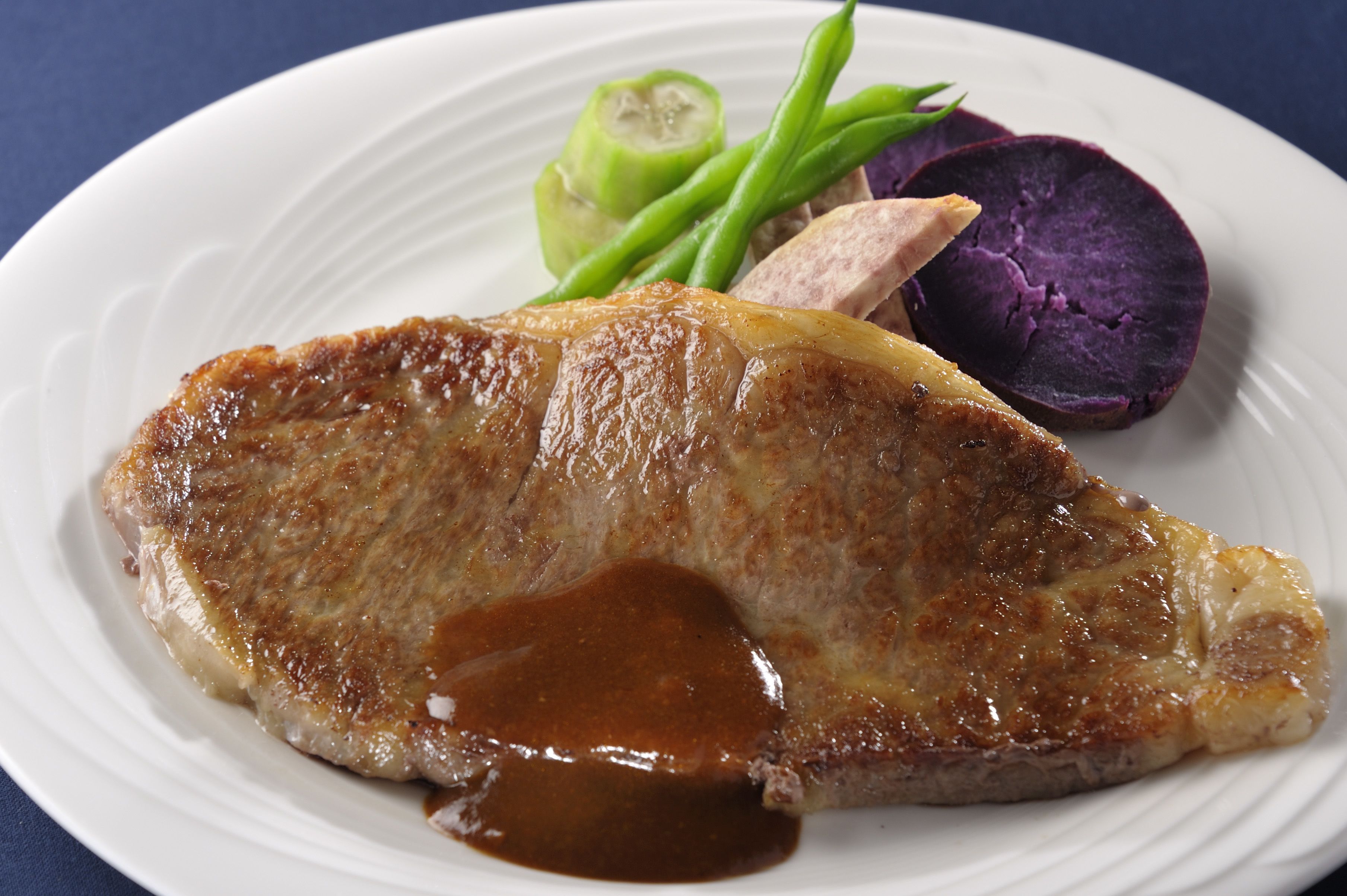 A plate with a grilled pork chop, green beans, and a slice of purple potato.
