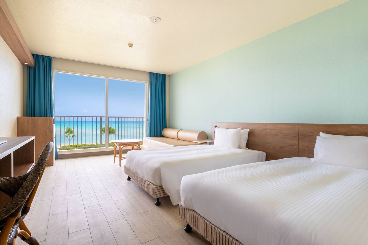 Habitación de hotel con dos camas, un escritorio y vista al océano.