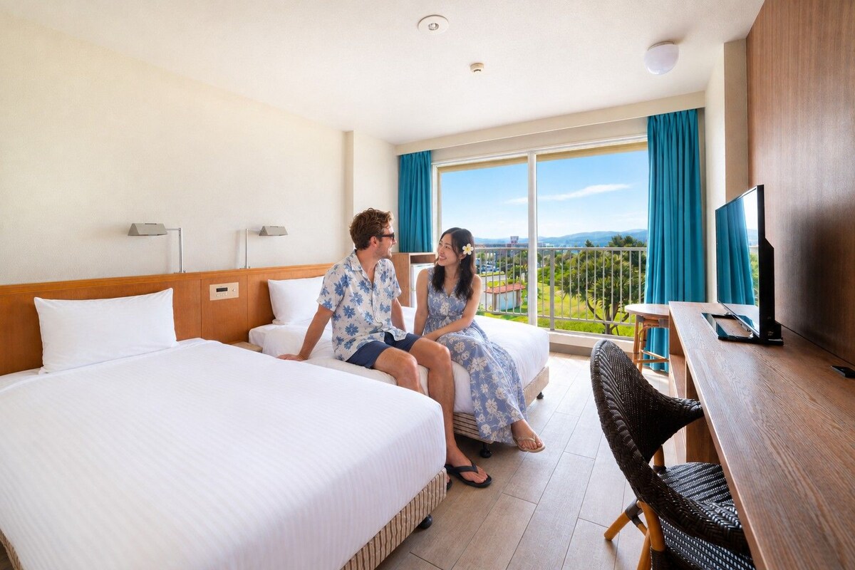 Habitación de hotel con cama, escritorio, televisor y balcón con vistas.