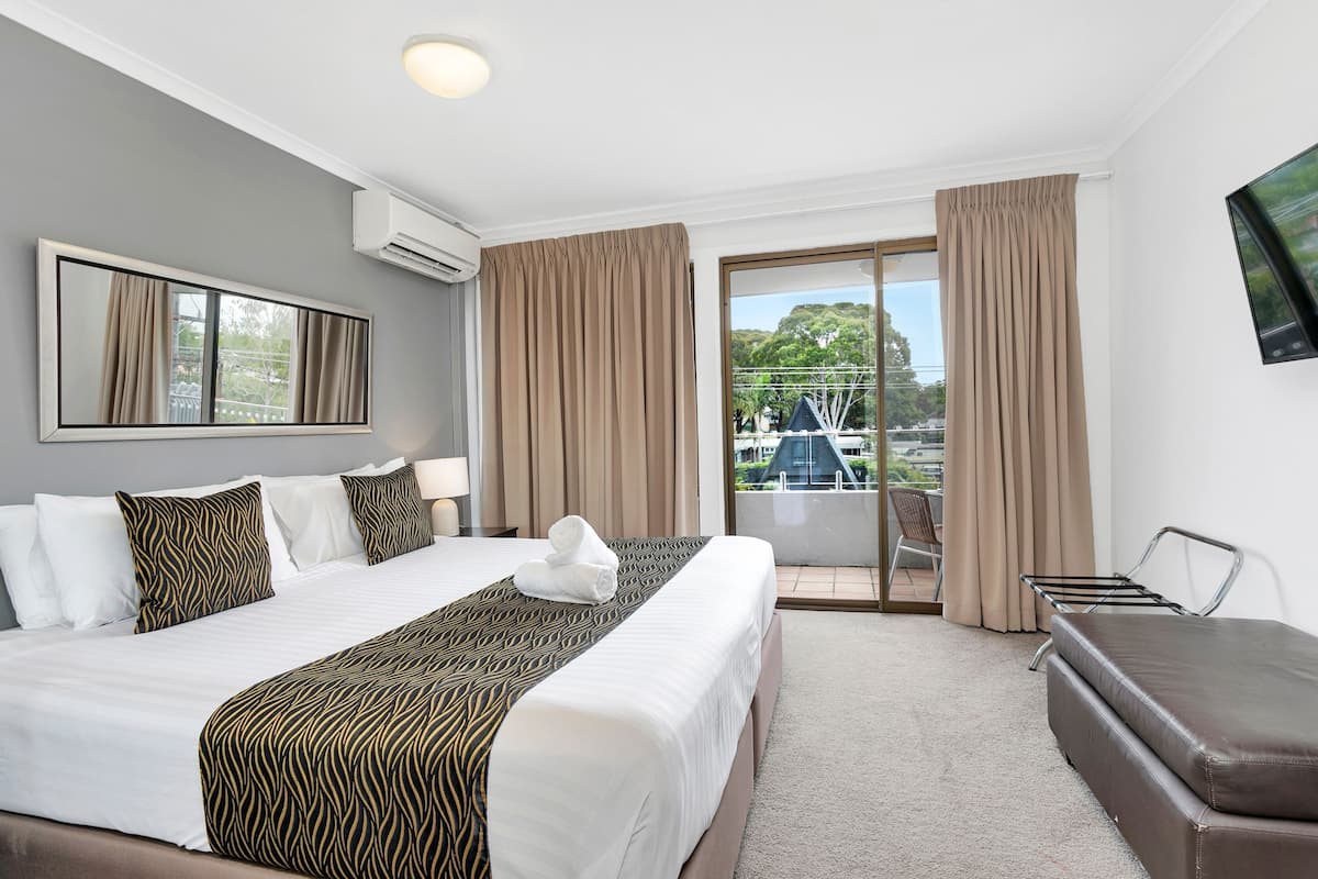Een hotelkamer met een groot bed, een bank, een televisie en een balkon met gordijnen.