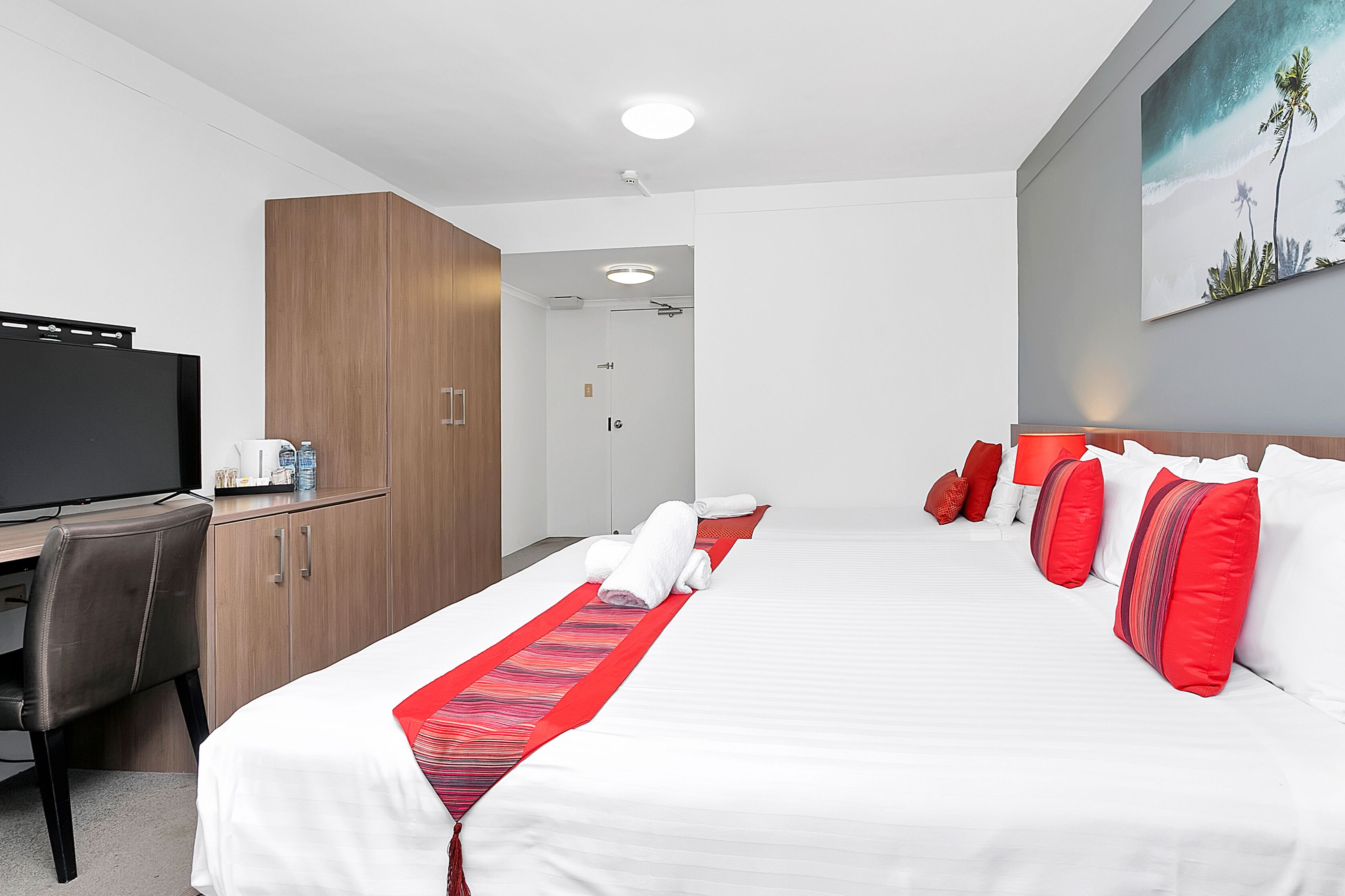 A hotel room with a bed, a desk, a television, and a painting on the wall.