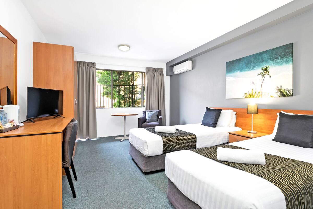 Een hotelkamer met twee bedden, een bureau met televisie, een klein tafeltje en een raam met gordijnen.