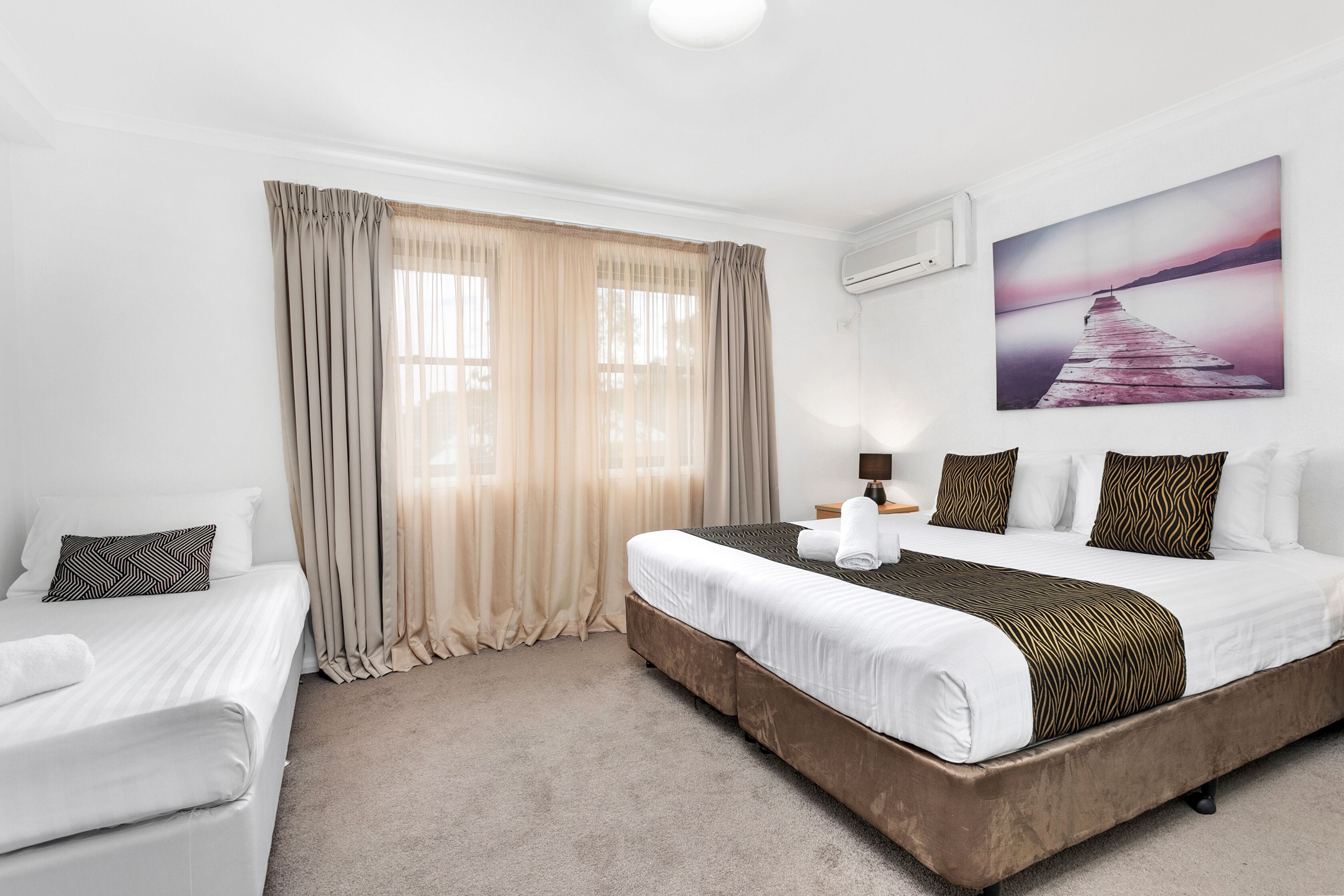 A hotel room with a large bed, a smaller bed, and a desk.
