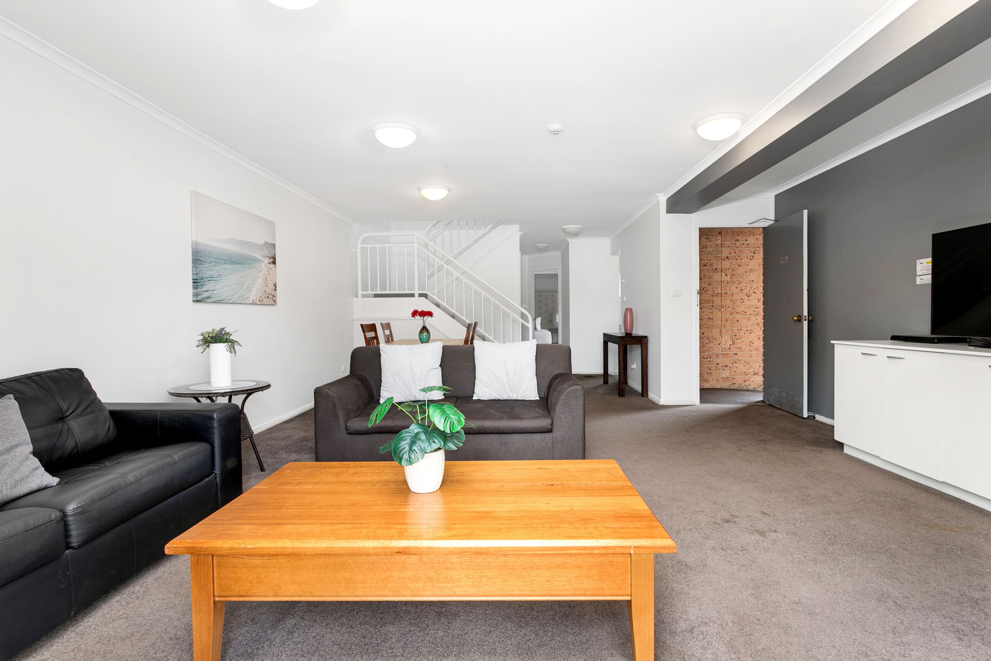 A modern living room with a black leather sofa, a wooden coffee table, and a grey carpet.