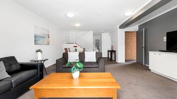 A modern living room with a black leather sofa, a wooden coffee table, and a grey carpet.
