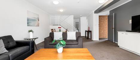 A modern living room with a black leather sofa, a wooden coffee table, and a grey carpet.